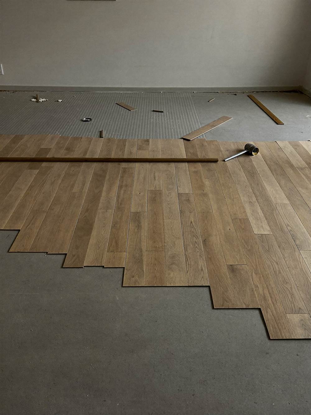 Oak parquet strips laid across most of a floor with a staggered leading edge, bare screed and a mallet beyond.